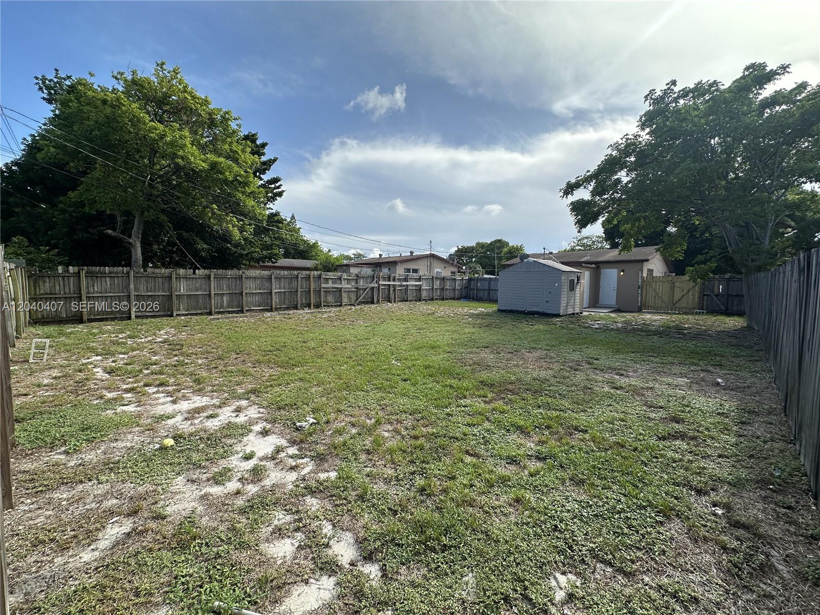 A fenced backyard features a grassy lawn, a small storage shed, and mature trees — 820 NW 4th Ave, Fort Lauderdale FL 33311, FORT LAUDERDALE, FL