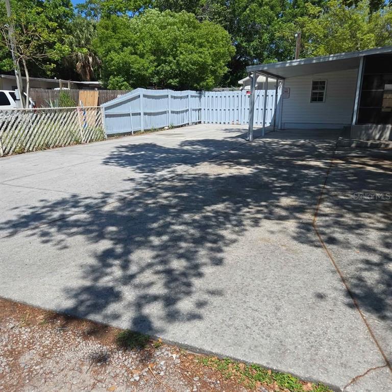 A concrete driveway leads to a covered carport beside a house with a blue fence — 4030 PECAN DRIVE, NEW PORT RICHEY, FL