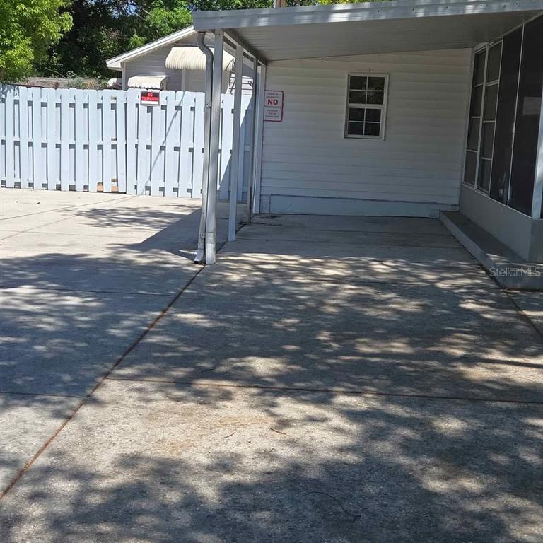A concrete driveway leads to a covered carport attached to a white-sided residential building — 4030 PECAN DRIVE, NEW PORT RICHEY, FL