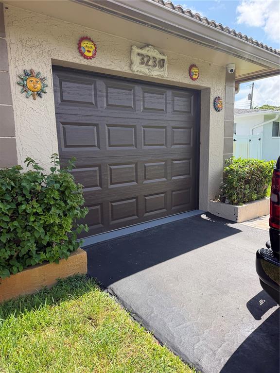 A dark brown garage door is framed by decorative sun ornaments and a house number plaque — 3230 HARRISON STREET, HOLLYWOOD, FL