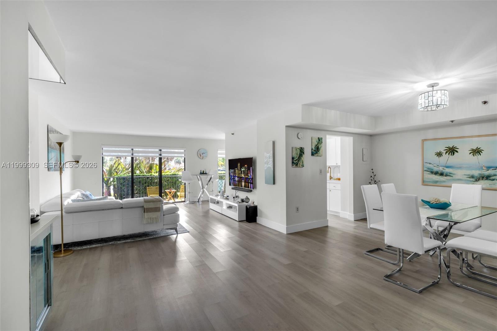 An open-concept living and dining area features light wood flooring, white furniture, and a balcony — 1201 S Ocean Dr # 110S, Hollywood FL 33019, HOLLYWOOD, FL