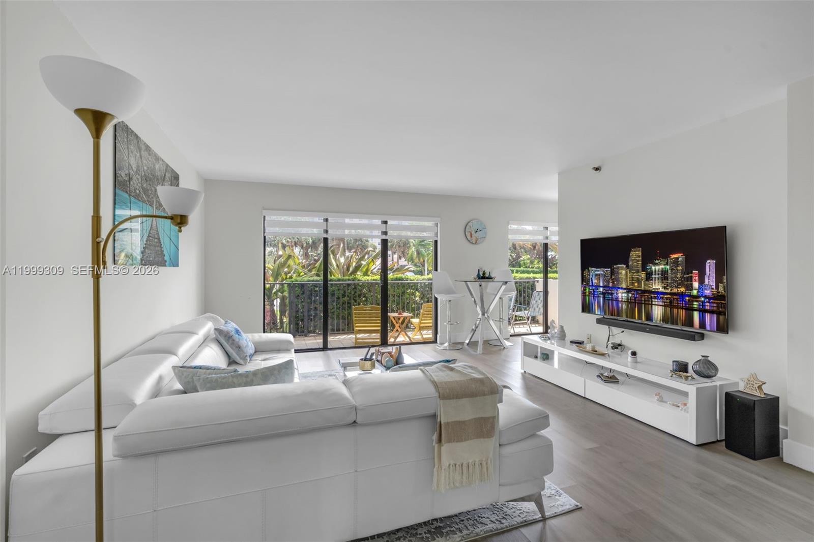A bright living room features a white sectional sofa, a wall-mounted television, and a balcony — 1201 S Ocean Dr # 110S, Hollywood FL 33019, HOLLYWOOD, FL