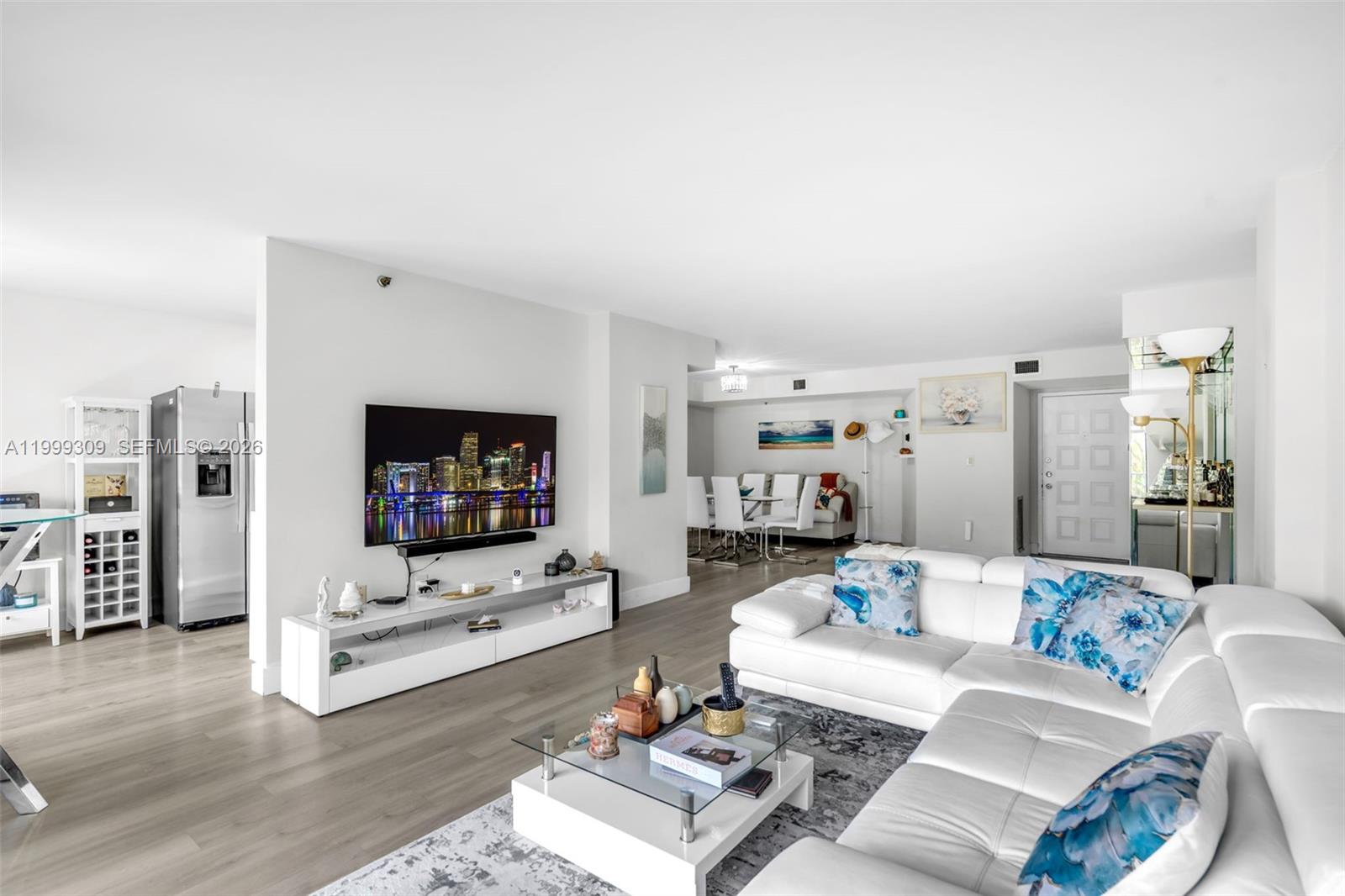 A bright living room features a white sectional sofa, a glass coffee table, and a television — 1201 S Ocean Dr # 110S, Hollywood FL 33019, HOLLYWOOD, FL