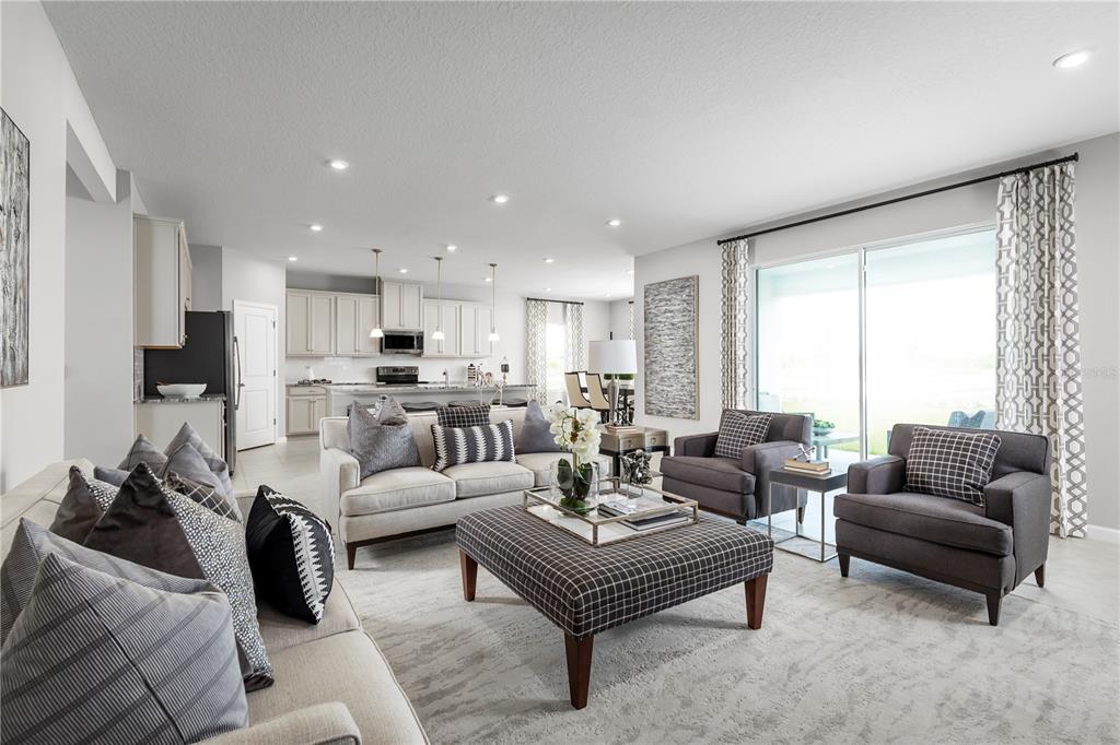 A bright, open-concept living room features neutral furniture, a large ottoman, and an adjacent kitchen — 11106 NELLIE CROSSING CIRCLE, CLERMONT, FL