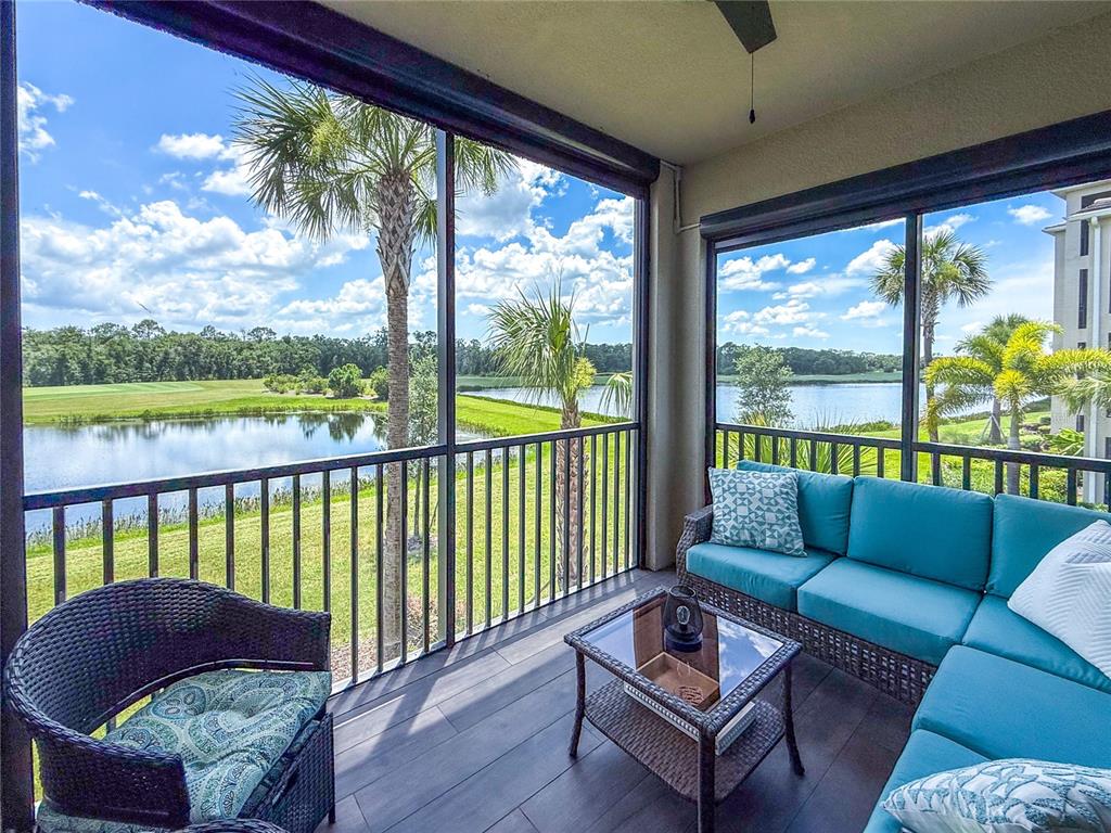 A screened-in balcony features wicker furniture, dark wood-look flooring, and a view of a lake — 17724 GAWTHROP DRIVE UNIT 208, BRADENTON, FL