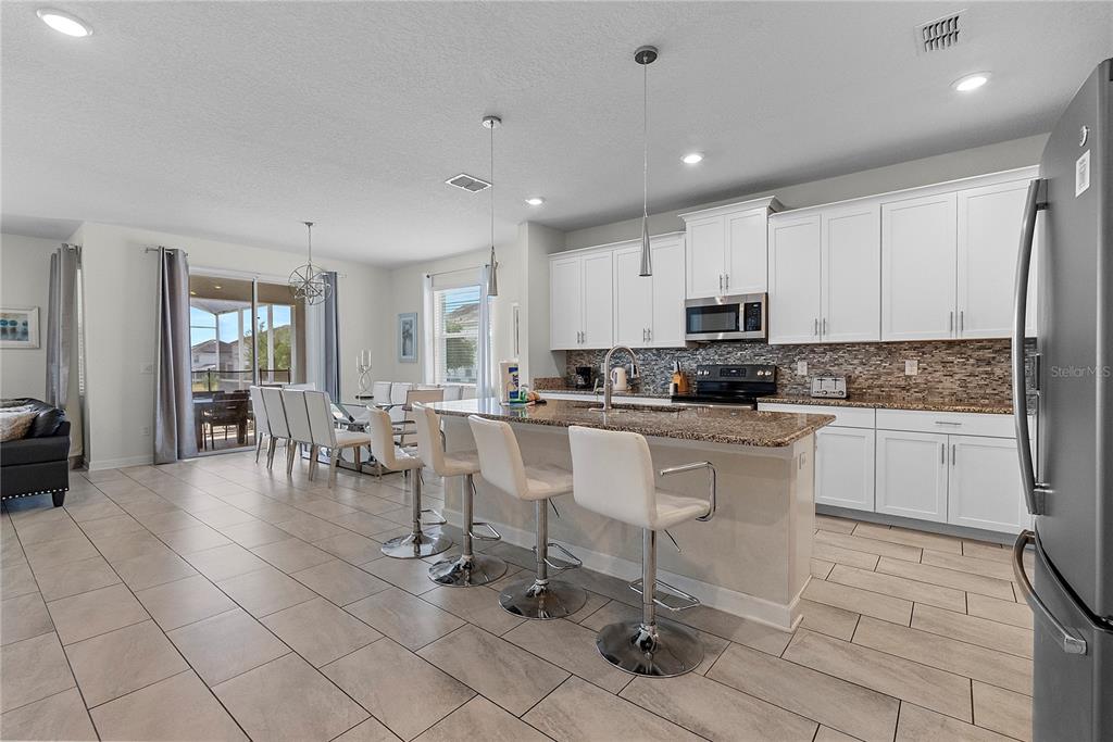 A kitchen with white cabinets, granite countertops, and an island with bar stools — 1559 FLANGE DRIVE, DAVENPORT, FL