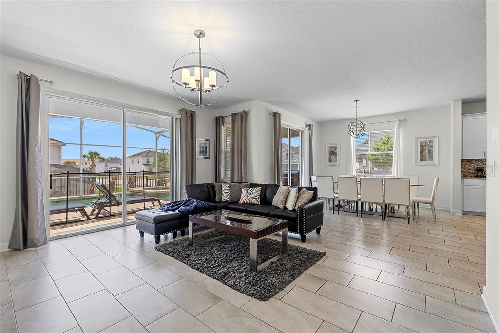An open-concept living and dining area features tile flooring, a black sectional, and pool views — 1559 FLANGE DRIVE, DAVENPORT, FL