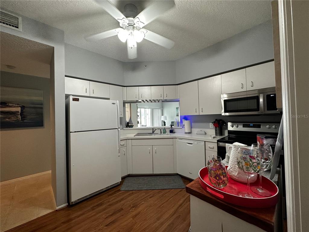 A kitchen with white cabinets, white appliances, and wood-look flooring under a ceiling fan — 5515 FAIR OAKS STREET UNIT 5515, BRADENTON, FL