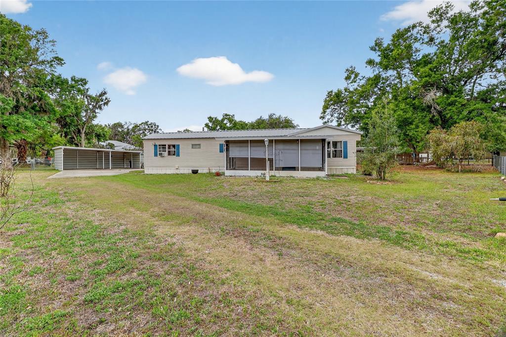 A single-story manufactured home with a screened porch and a detached metal carport — 4710 VILLAGE DRIVE, LAKELAND, FL