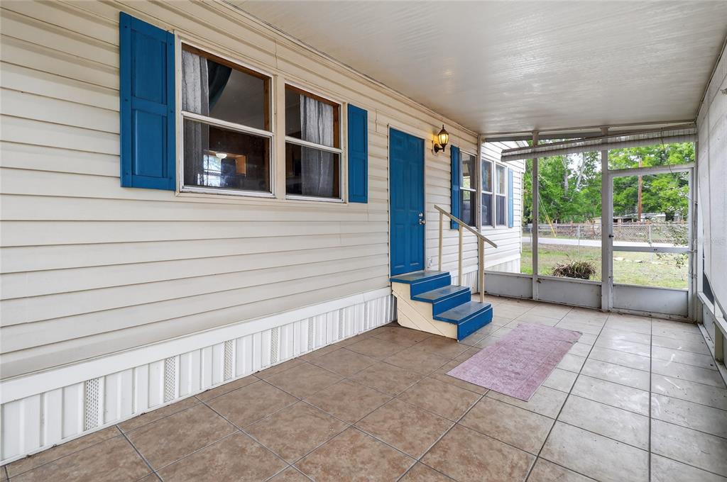 A covered porch with tiled flooring, blue steps, and a blue door on a mobile home — 4710 VILLAGE DRIVE, LAKELAND, FL