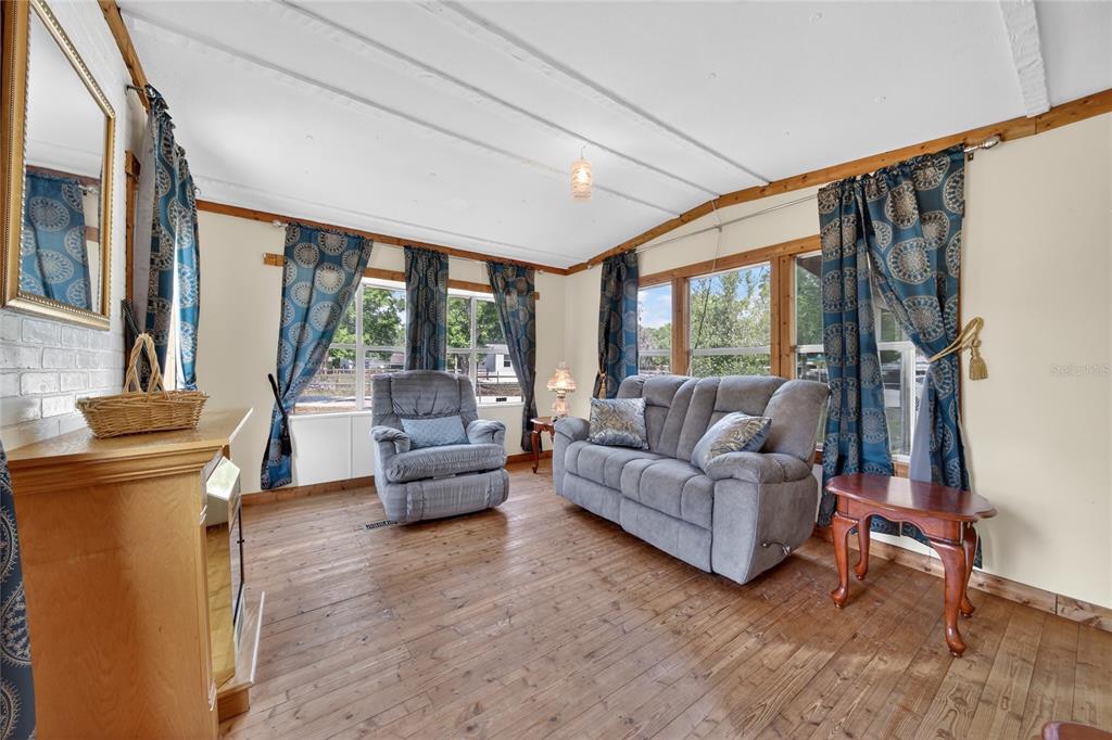 A living room features wood flooring, a gray sofa, a recliner, and blue patterned curtains — 4710 VILLAGE DRIVE, LAKELAND, FL