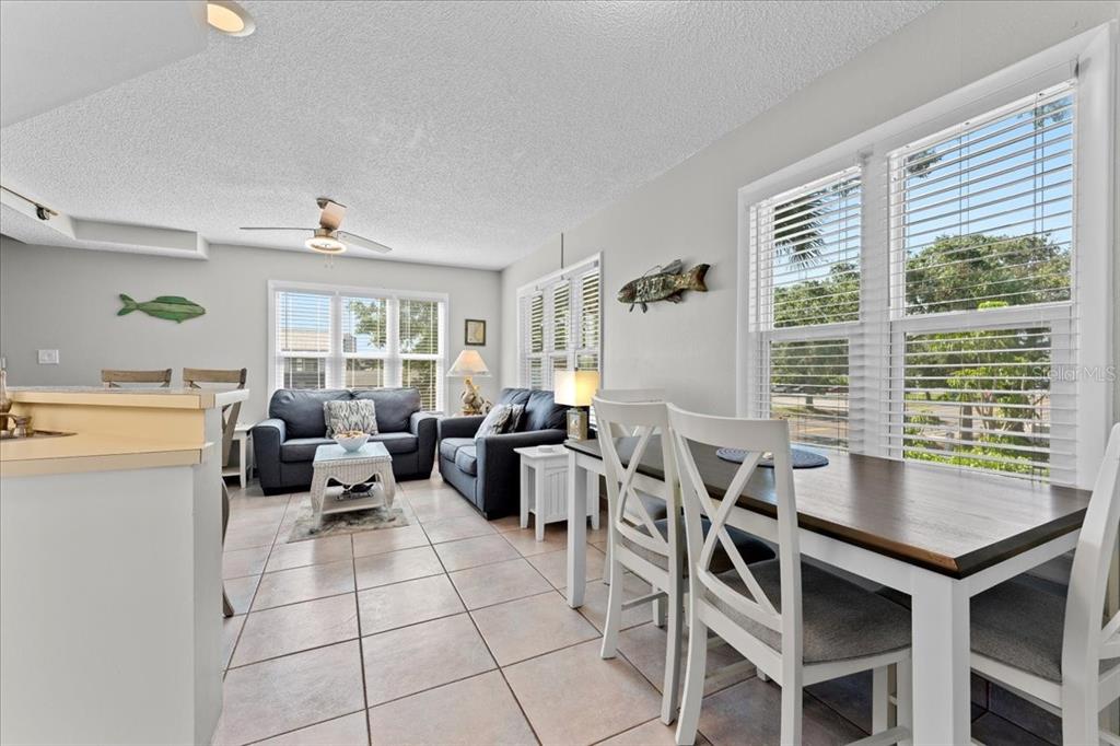 An open-concept living and dining area features tile flooring, neutral walls, and large windows — 112 GULF BOULEVARD UNIT A, INDIAN ROCKS BEACH, FL