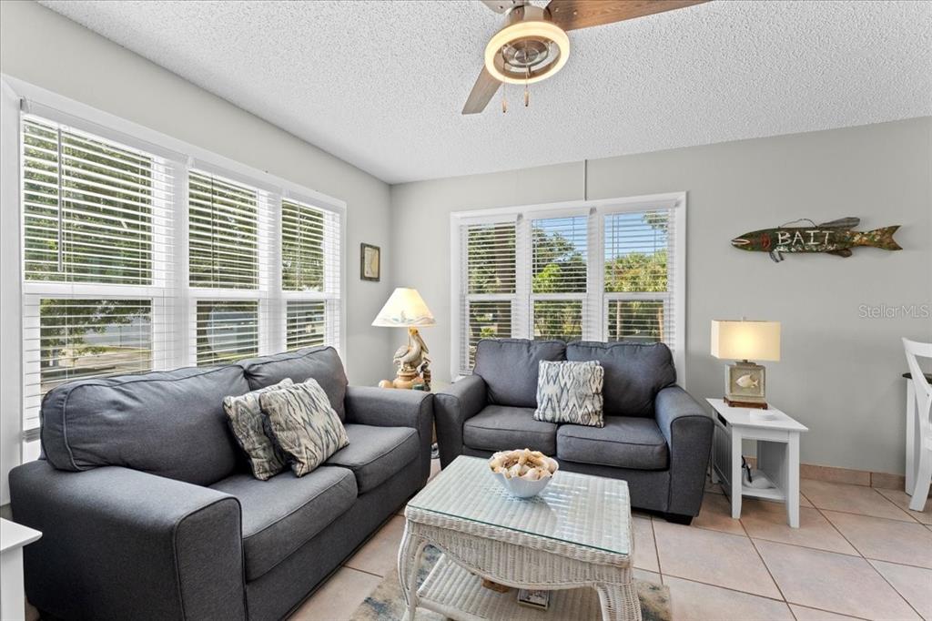 A living room features two gray sofas, a glass-topped coffee table, and tile flooring — 112 GULF BOULEVARD UNIT A, INDIAN ROCKS BEACH, FL