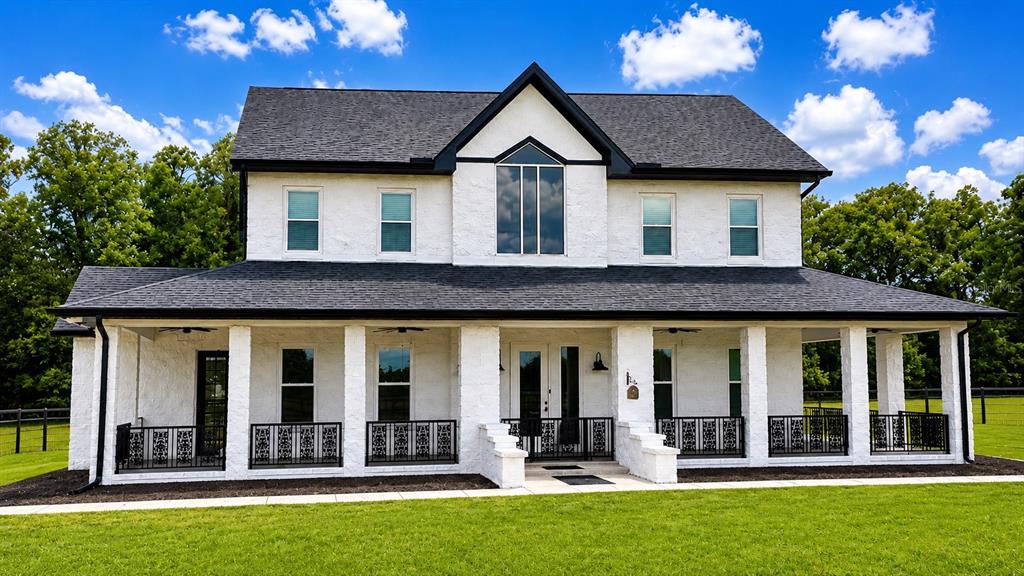 A two-story white brick house with a dark roof and a wrap-around front porch — 5440 NE 31ST TERRACE, OCALA, FL