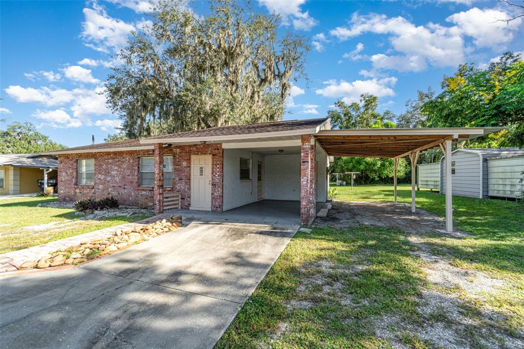 A single-story brick house with a concrete driveway, a carport, and a large shade tree — 918 W MAGNOLIA STREET, ARCADIA, FL