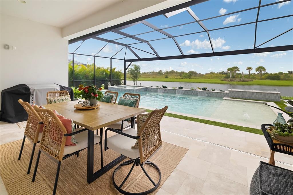 A covered patio features a dining set overlooking a screened-in swimming pool and a lake — 17128 RANCHSIDE PLACE, LAKEWOOD RANCH, FL