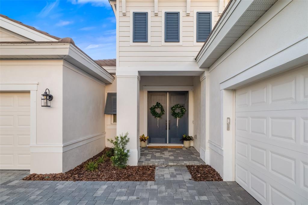 A front exterior view of a house with double doors, a paver driveway, and garage — 17128 RANCHSIDE PLACE, LAKEWOOD RANCH, FL
