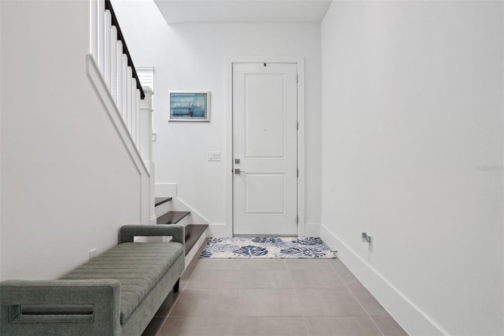 An entryway features a gray bench, tiled floor, white walls, and a staircase with railings — 12566 WESTHAVEN OAK DRIVE, WINTER GARDEN, FL