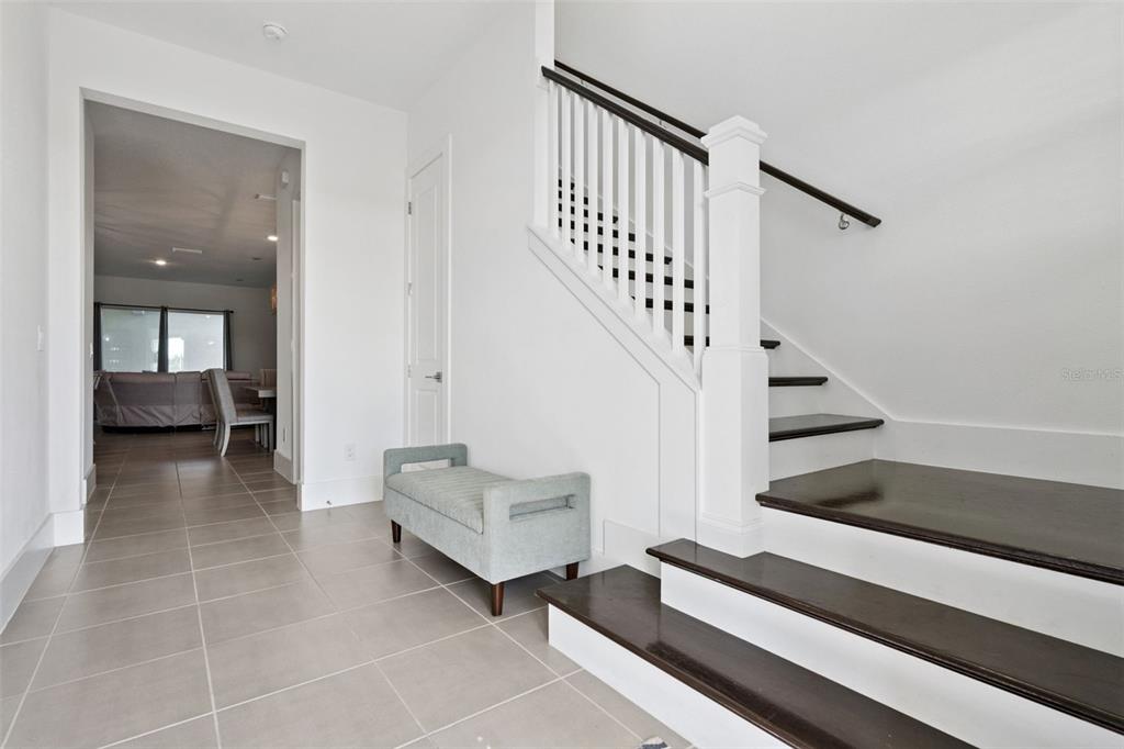 A bright entryway features a staircase with dark wood treads and a light blue bench — 12566 WESTHAVEN OAK DRIVE, WINTER GARDEN, FL