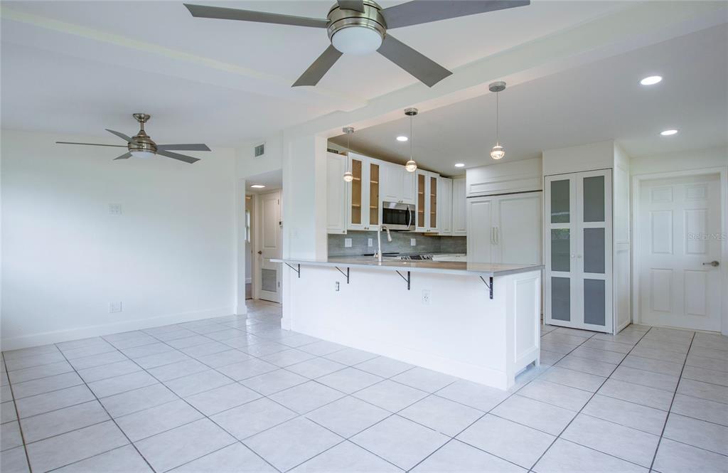 A bright kitchen with white cabinets and a breakfast bar opens to a tiled room — 10276 121ST AVENUE, LARGO, FL