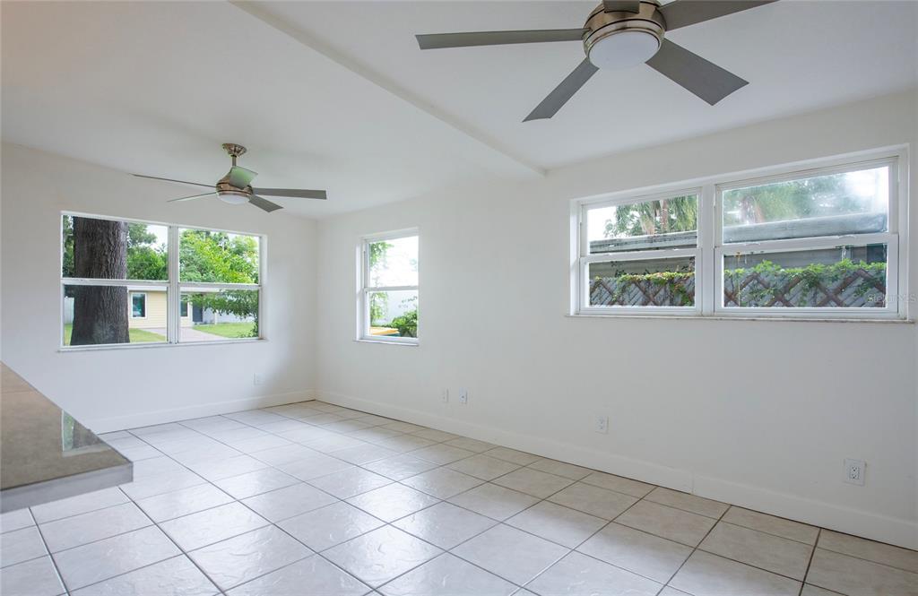 An empty room with white walls, tiled floors, two ceiling fans, and several windows — 10276 121ST AVENUE, LARGO, FL