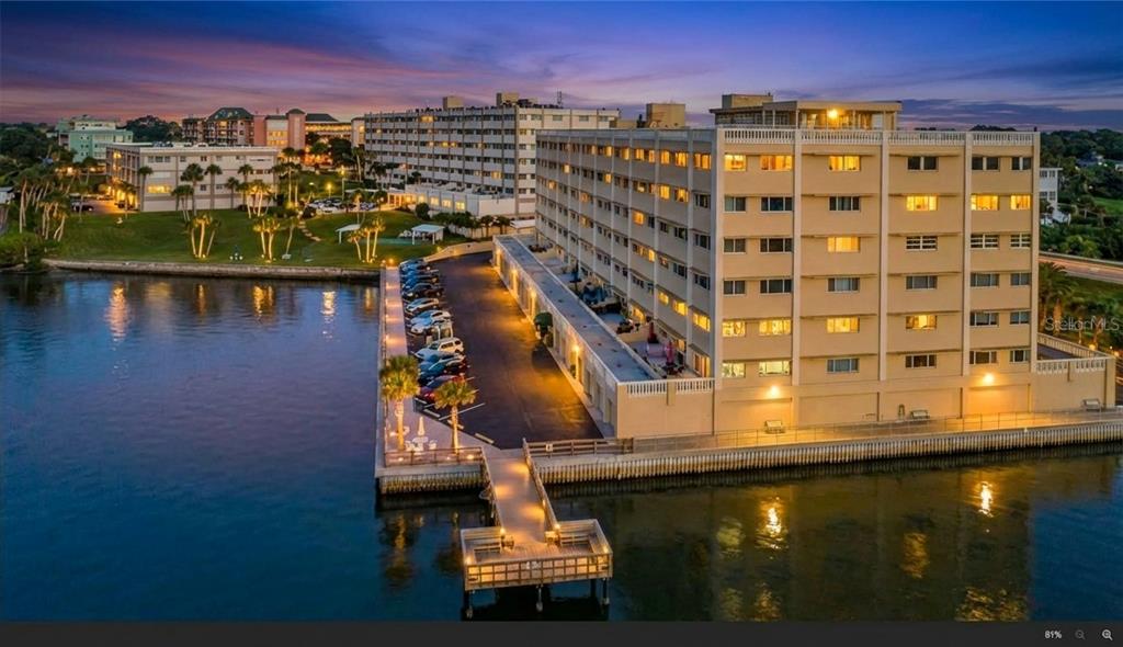 An aerial view of a multi-story waterfront apartment building with an attached parking lot and pier — 100 BLUFF VIEW DRIVE UNIT 608C, BELLEAIR BLUFFS, FL