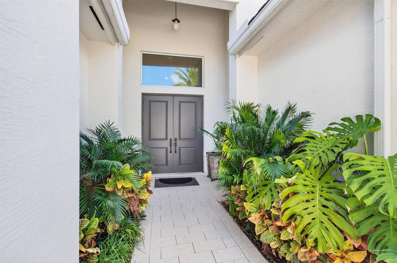 A paved walkway leads to a gray double-door entryway flanked by lush tropical plants — 19886 Meadowside Lane Lane, Boca Raton FL 33498, BOCA RATON, FL