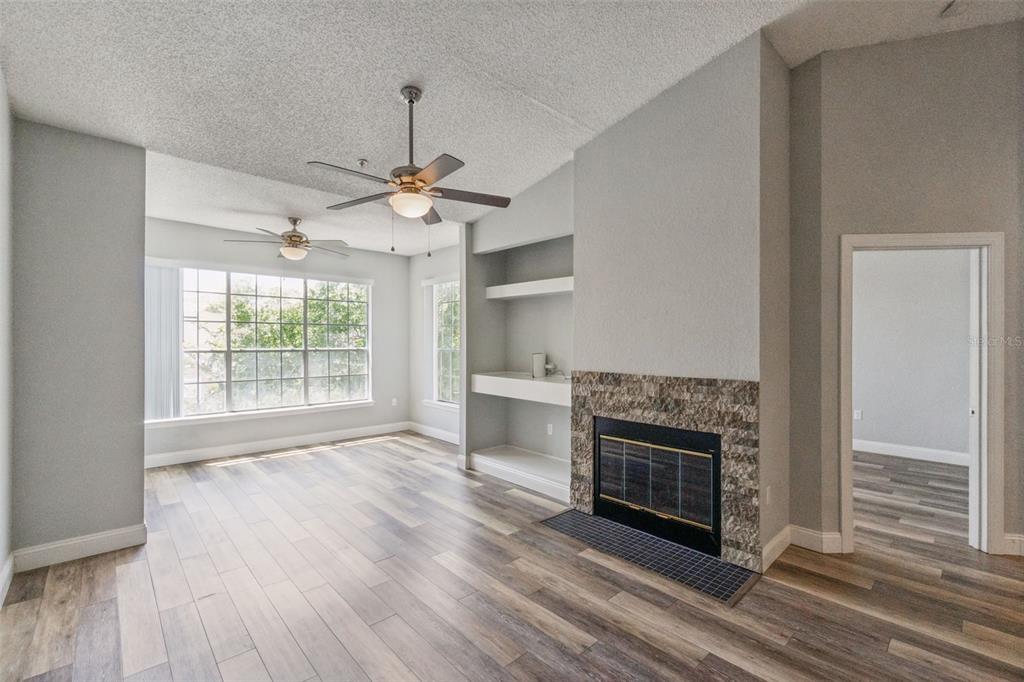A living room features wood-look flooring, a stone fireplace, built-in shelving, and two ceiling fans — 13015 PLANTATION PARK CIRCLE UNIT 1035, ORLANDO, FL