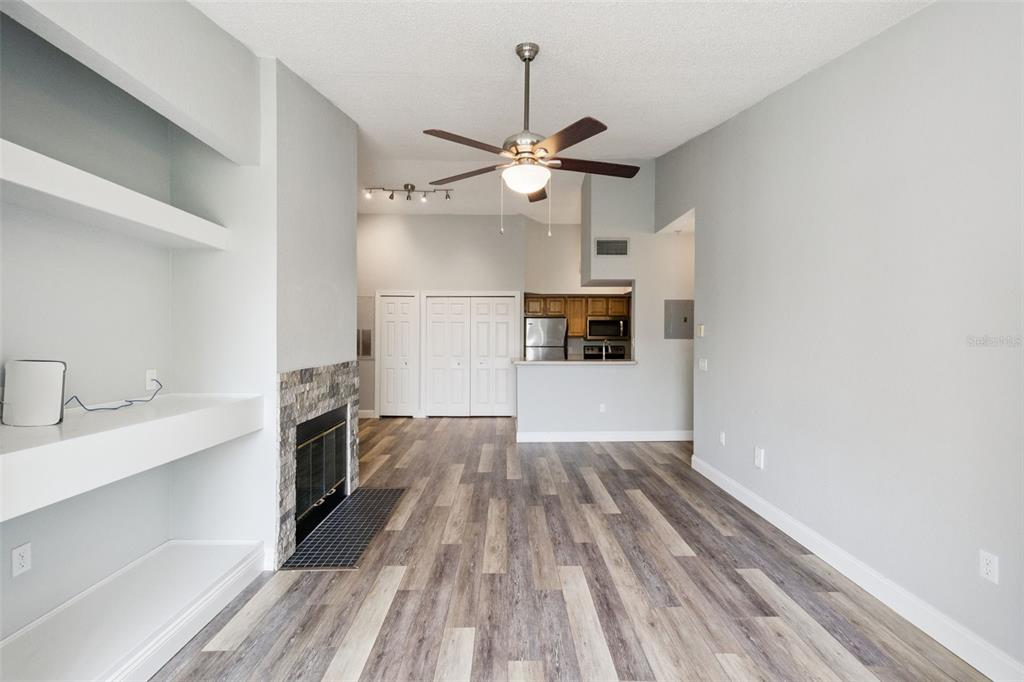 A living room with wood-look flooring, a stone-faced fireplace, built-in shelving, and an open kitchen — 13015 PLANTATION PARK CIRCLE UNIT 1035, ORLANDO, FL