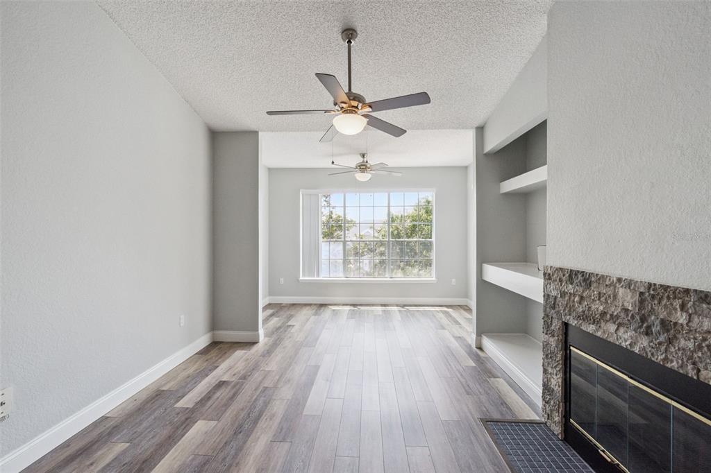 A living room features wood-look flooring, a stone fireplace, built-in shelves, and two ceiling fans — 13015 PLANTATION PARK CIRCLE UNIT 1035, ORLANDO, FL