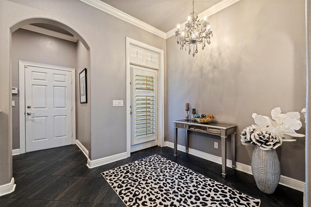 A foyer features dark wood-look flooring, a crystal chandelier, a mirrored console table, and shutters — 618 SAXONY BOULEVARD, ST PETERSBURG, FL