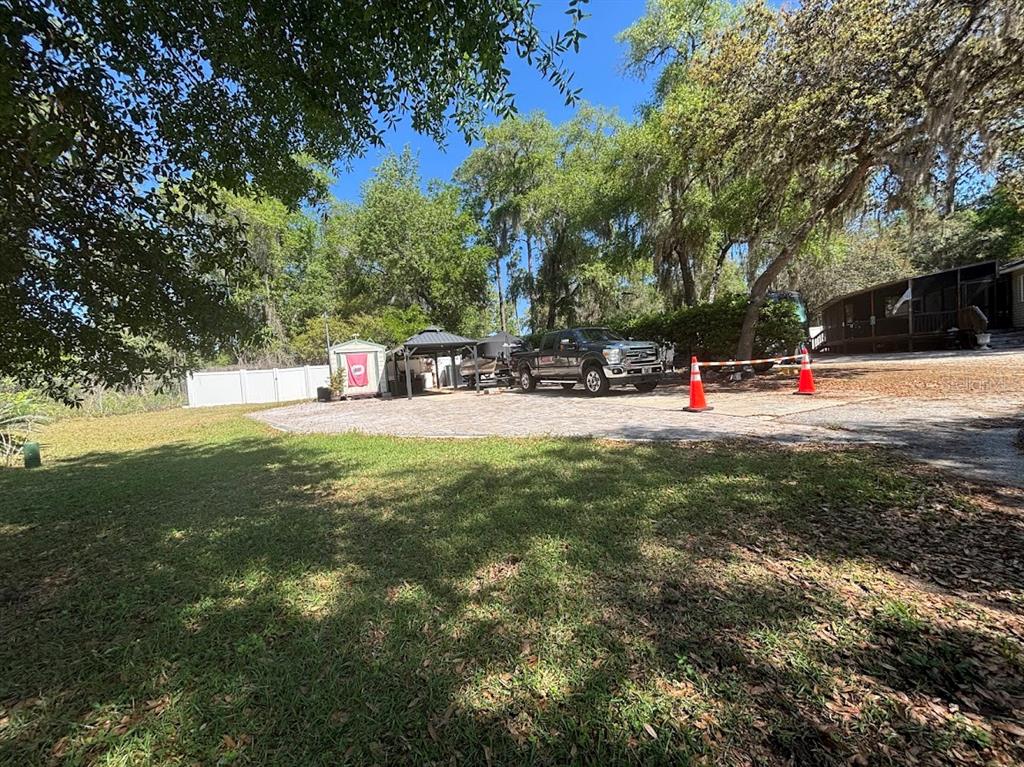 A gravel driveway features a parked truck, a small shed, and a gazebo near trees — 14415 252ND COURT ROAD NE UNIT 133, FORT MC COY, FL