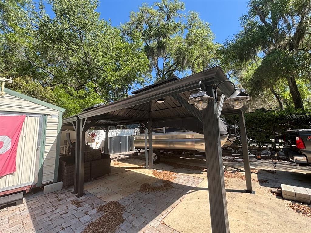 A metal gazebo covers a paved patio area next to a shed and a boat trailer — 14415 252ND COURT ROAD NE UNIT 133, FORT MC COY, FL