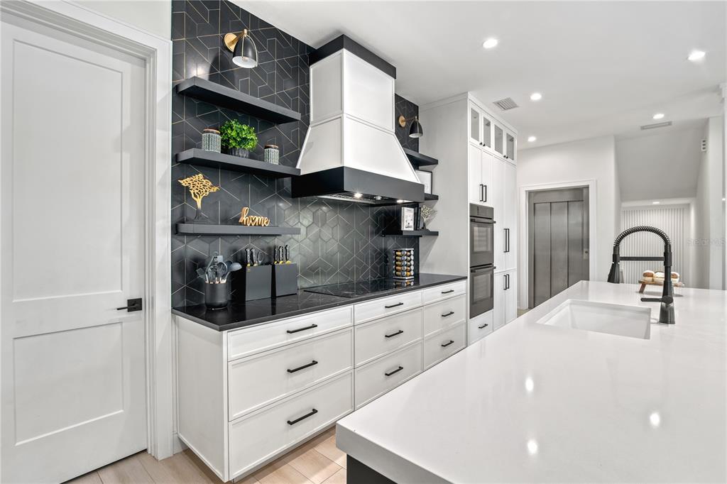 A modern kitchen features white cabinetry, a black geometric tile backsplash, and a large island — 129 MCKINLEY DRIVE, SARASOTA, FL
