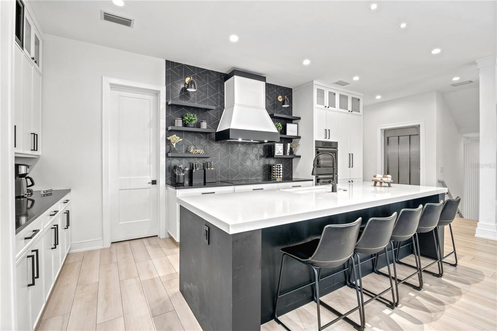 A modern kitchen features a large black island, white cabinetry, and a geometric-tiled backsplash — 129 MCKINLEY DRIVE, SARASOTA, FL