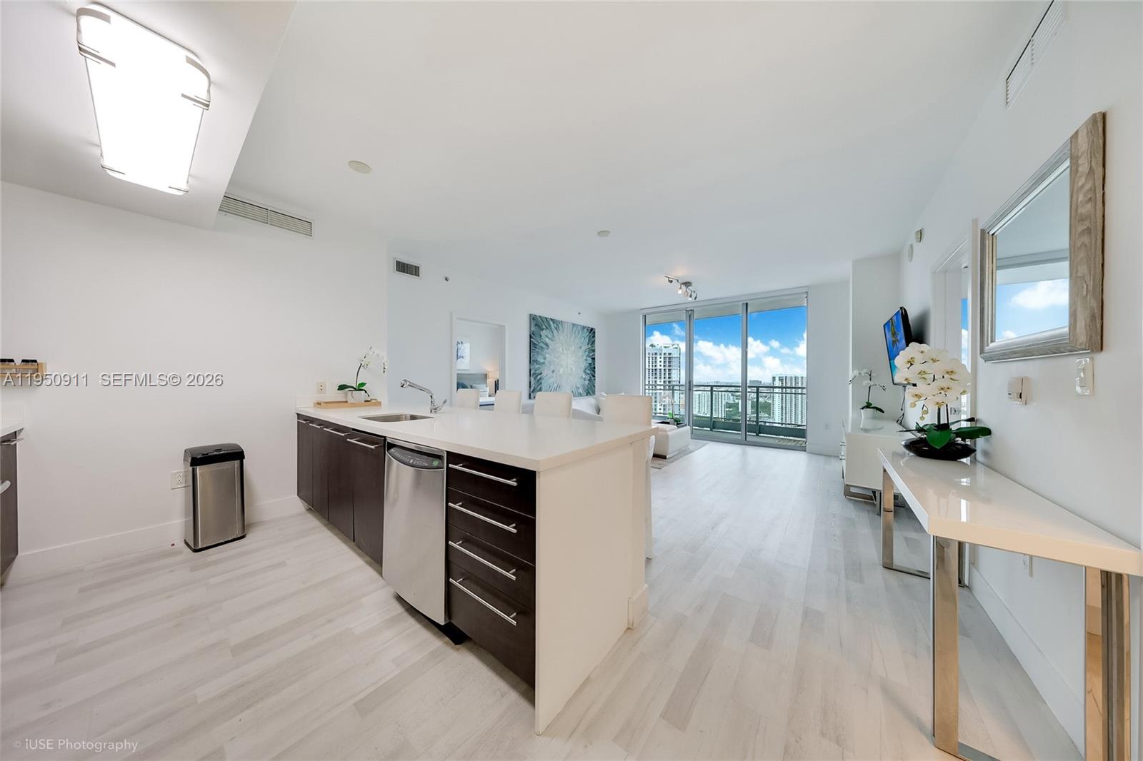 A modern kitchen with a white island and dark cabinets opens into a bright living area — 90 SW 3rd St # 3109, Miami FL 33130, MIAMI, FL