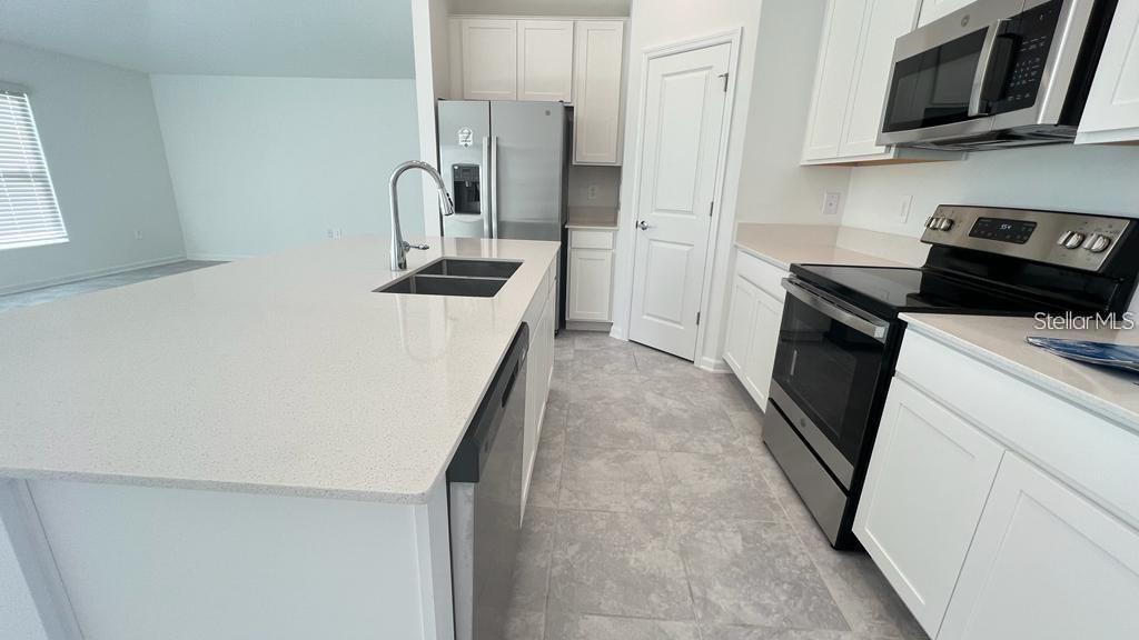A kitchen features white cabinets, stainless steel appliances, a large island, and light-colored tile flooring — 263 BRAVE ROAD, DAVENPORT, FL