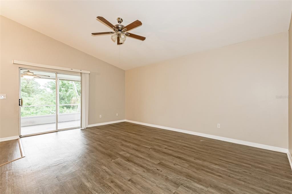 An empty living room features light-colored walls, wood-look flooring, a ceiling fan, and sliding glass doors — 823 ROCKY MOUNTAIN COURT, VALRICO, FL