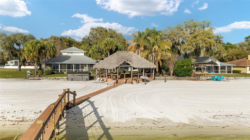 A sandy beach leads to a wooden dock, a thatched-roof gazebo, and waterfront houses — 14261 SE 128TH STREET, OCKLAWAHA, FL