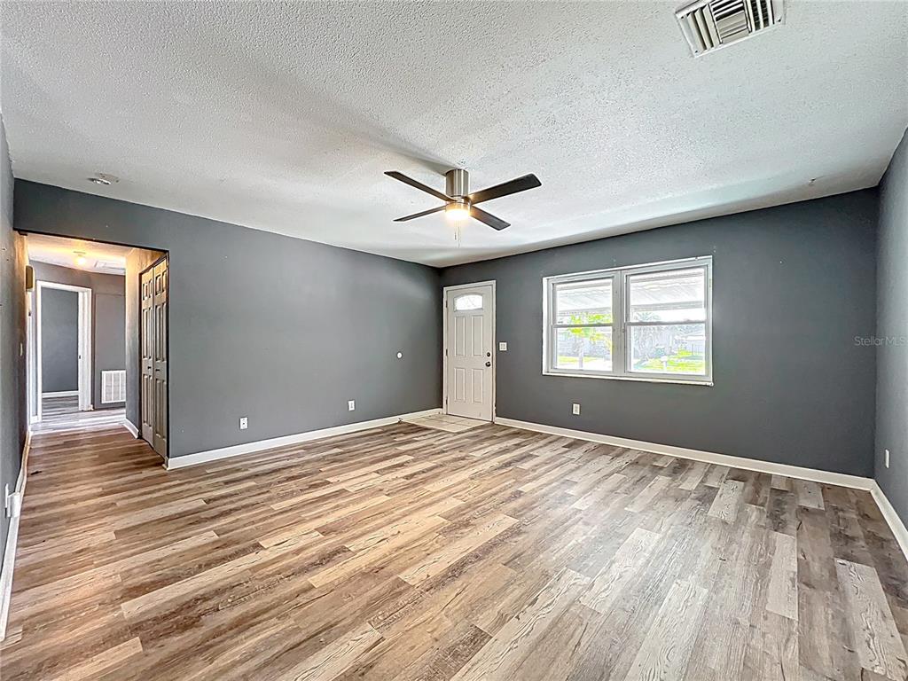 An empty living room features dark gray walls, wood-look flooring, a ceiling fan, and windows — 2543 HATHAWAY DRIVE, COCOA, FL