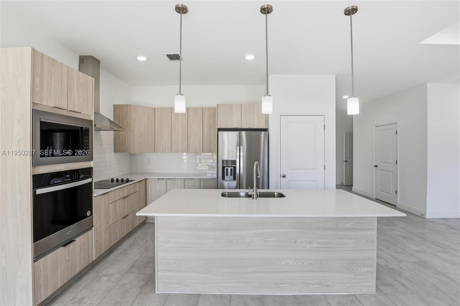 A modern kitchen features light wood cabinets, stainless steel appliances, and a large white island — 1087 Rugby Ln, La Belle FL 33935, LA BELLE, FL