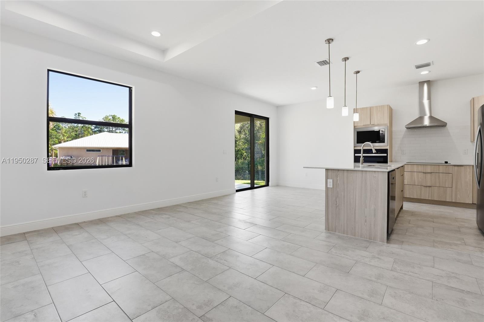 A modern, open-concept kitchen and living area features light wood cabinets and tile flooring — 1087 Rugby Ln, La Belle FL 33935, LA BELLE, FL