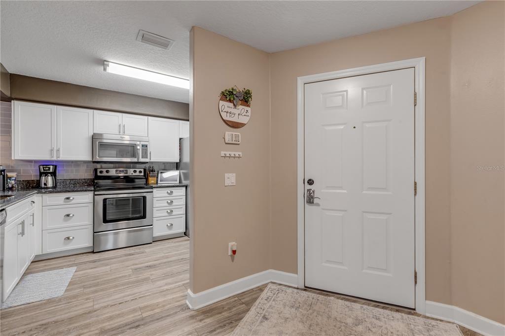 A white front door opens into a kitchen with white cabinets and stainless steel appliances — 24 GOLF VILLA DRIVE, PORT ORANGE, FL