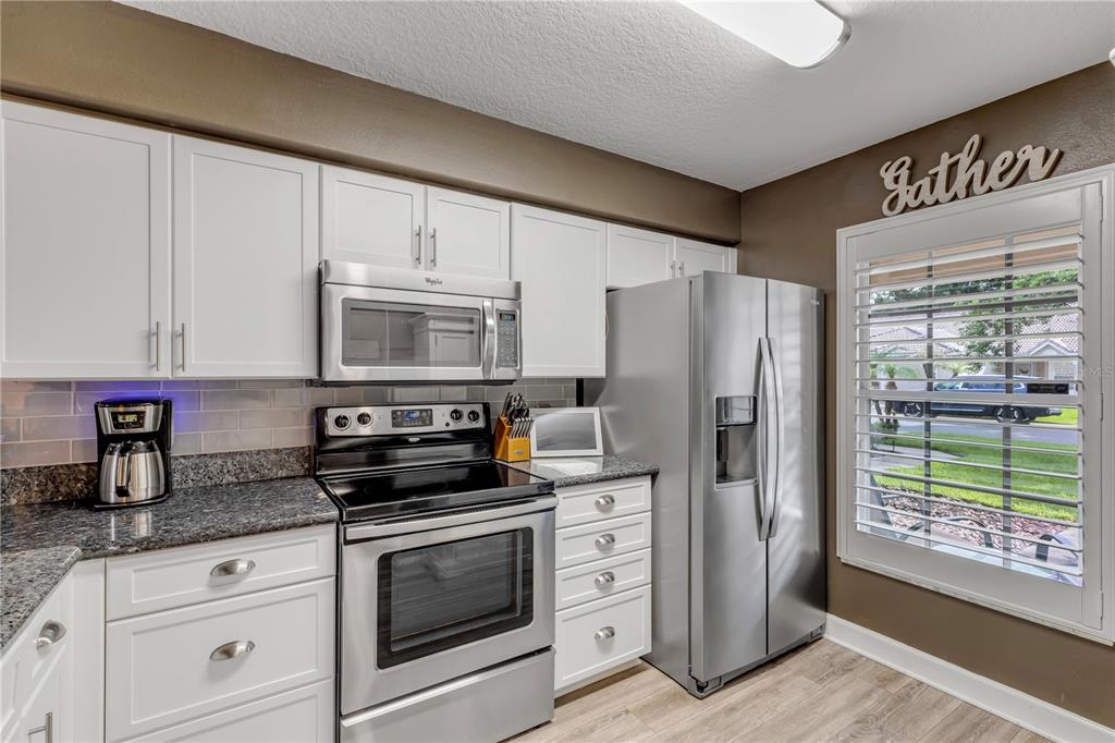 A kitchen features white cabinets, stainless steel appliances, granite countertops, and a window with shutters — 24 GOLF VILLA DRIVE, PORT ORANGE, FL