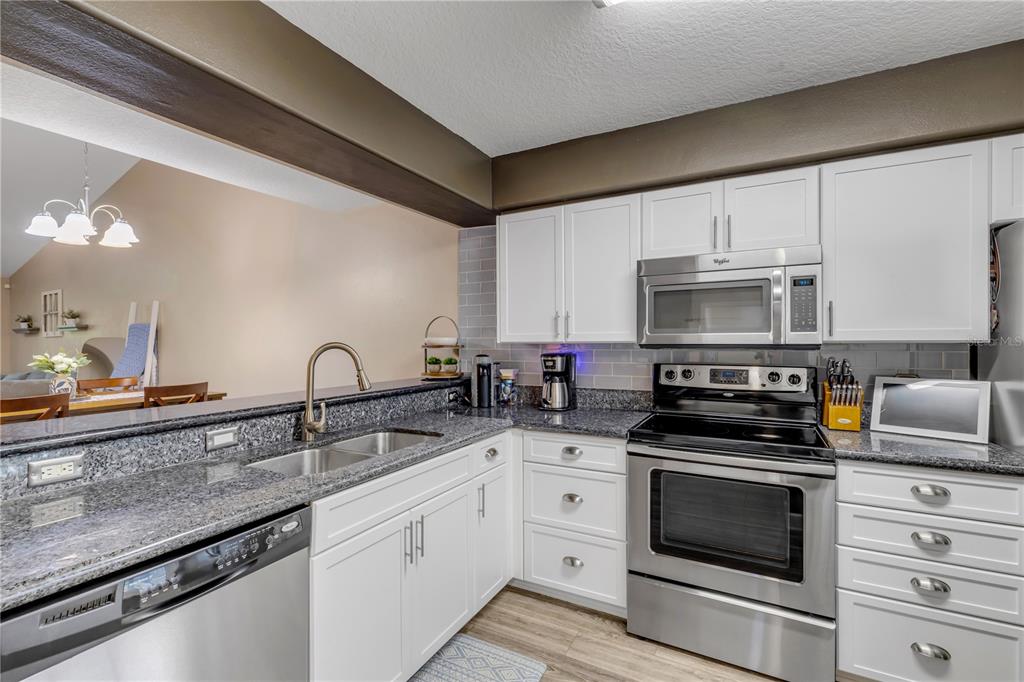 A kitchen features white cabinets, granite countertops, stainless steel appliances, and a gray tile backsplash — 24 GOLF VILLA DRIVE, PORT ORANGE, FL