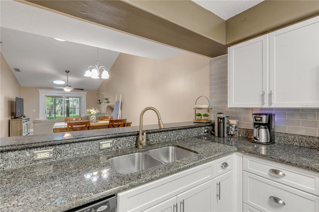 A kitchen with granite countertops, white cabinets, and a view into the dining area — 24 GOLF VILLA DRIVE, PORT ORANGE, FL
