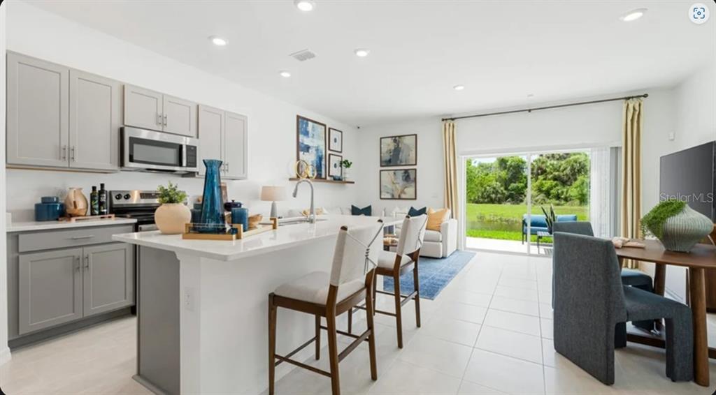 An open-concept living room and kitchen area with light walls, tile floors, and gray cabinetry — 7154 GRAND FOREST WAY, NOKOMIS, FL