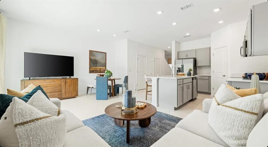 A living room features a white sectional sofa, a round wooden coffee table, and wall art — 7154 GRAND FOREST WAY, NOKOMIS, FL
