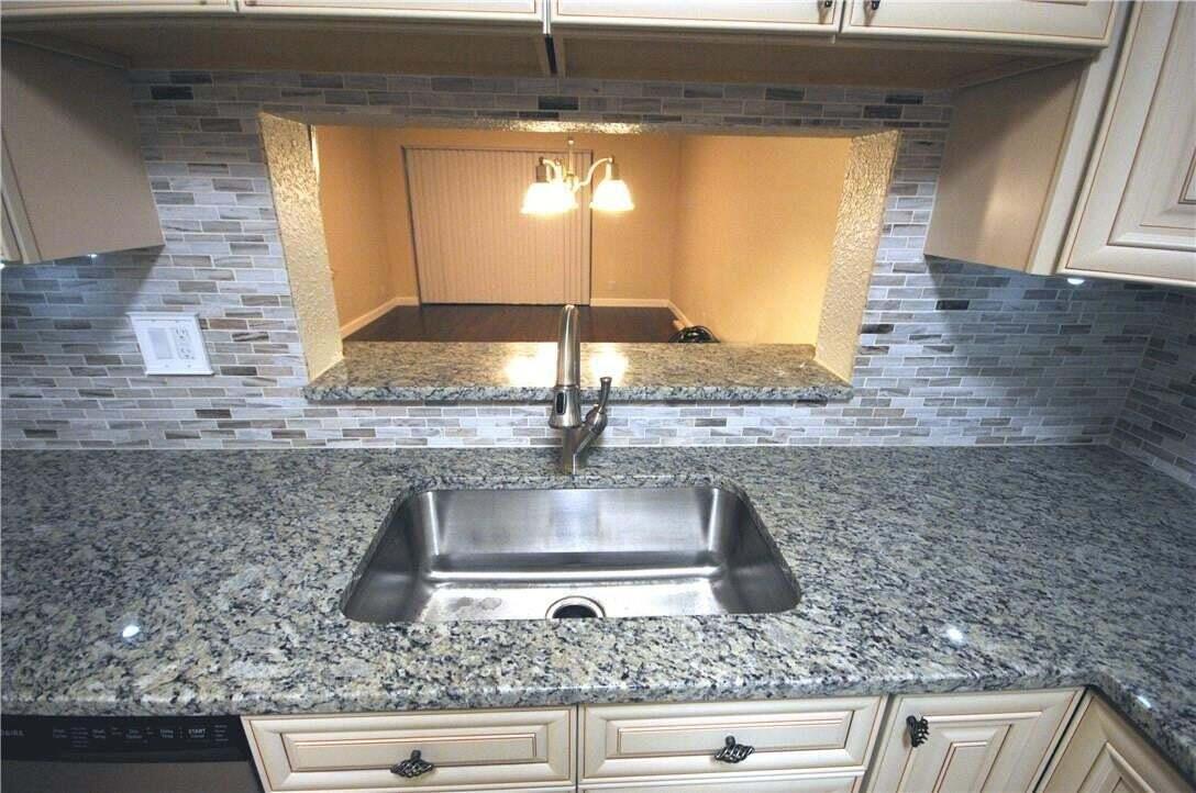 A kitchen sink with a granite countertop and tiled backsplash overlooks an adjacent room — 3071 Holiday Springs Boulevard # 101, Margate FL 33063, MARGATE, FL