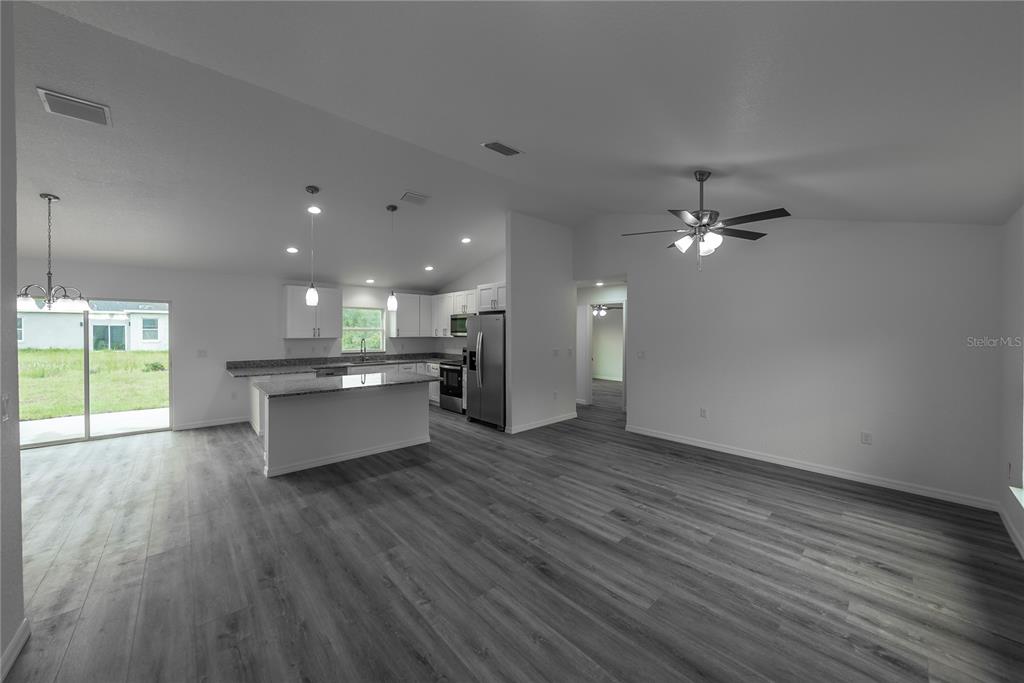 An open-concept kitchen and living area features gray wood-look flooring and white cabinetry — 11 MALAUKA PASS, OCKLAWAHA, FL
